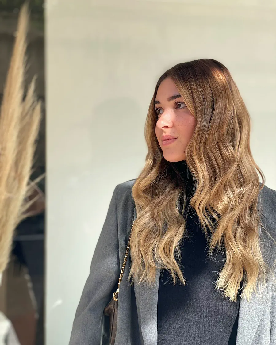 Melena larga castaña con las puntas más claras, peinada en ondas.